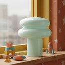 Pastel green lamp on a table with colorful toys against a window and star-patterned curtain.