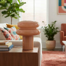 Decorative lamp on a wooden table in a living room with a couch, books, and plants.