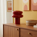 Decorative red vase on a wooden cabinet with abstract wall art in the background