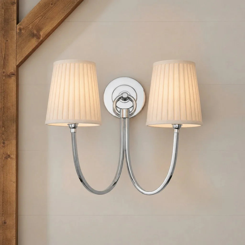 Double wall sconce with pleated lampshades on a neutral wall.