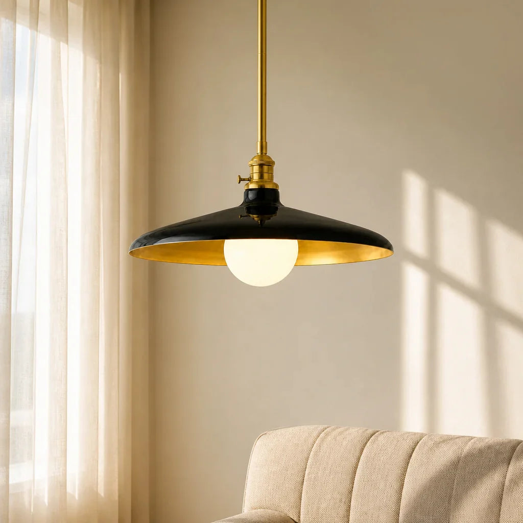 Pendant light with black shade and gold trim hanging in a room with beige curtains and sofa.