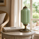 Decorative green urn with gold accents on a wooden table near a window.