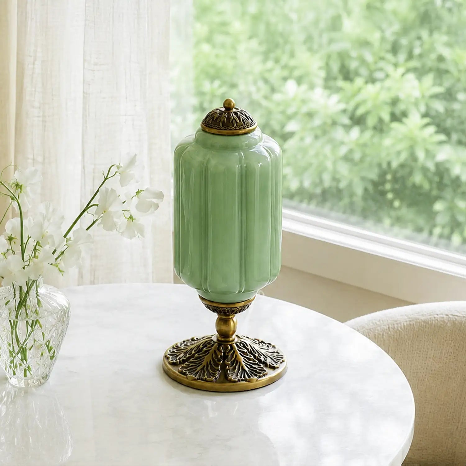 Green ceramic vase with gold base on a table near a window with white curtains