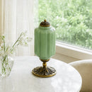 Green ceramic vase with gold base on a table near a window with white curtains