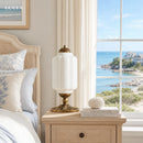 Bedroom with a bedside table, lamp, and view of the ocean through a window.