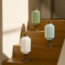Three decorative lamps with green, white, and gold bases on a wooden shelf.