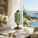 Green lamp on a table with a scenic view of a pool and ocean.