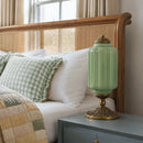 Green lamp with gold base on a nightstand next to a bed with pillows and a quilt.