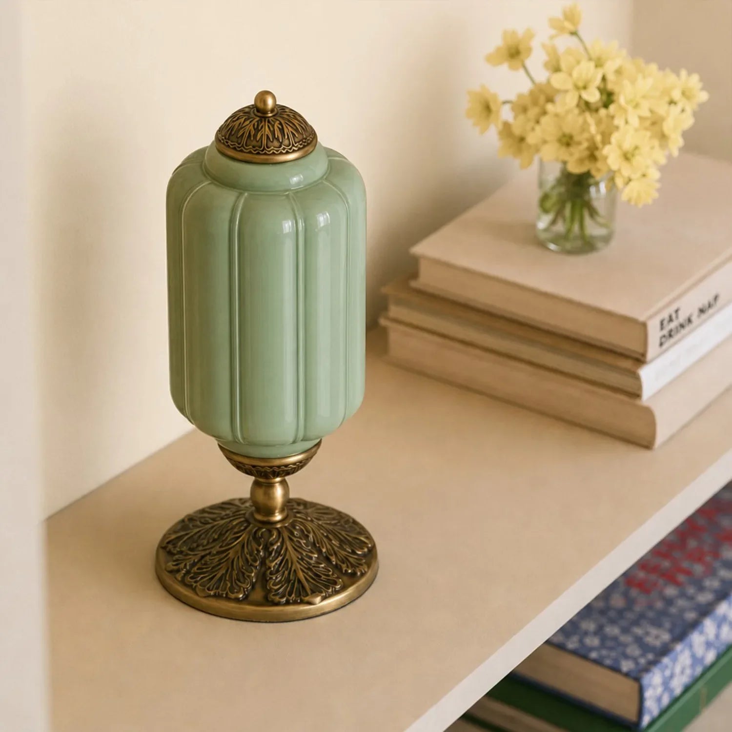 Decorative green and gold lamp on a shelf with books and flowers