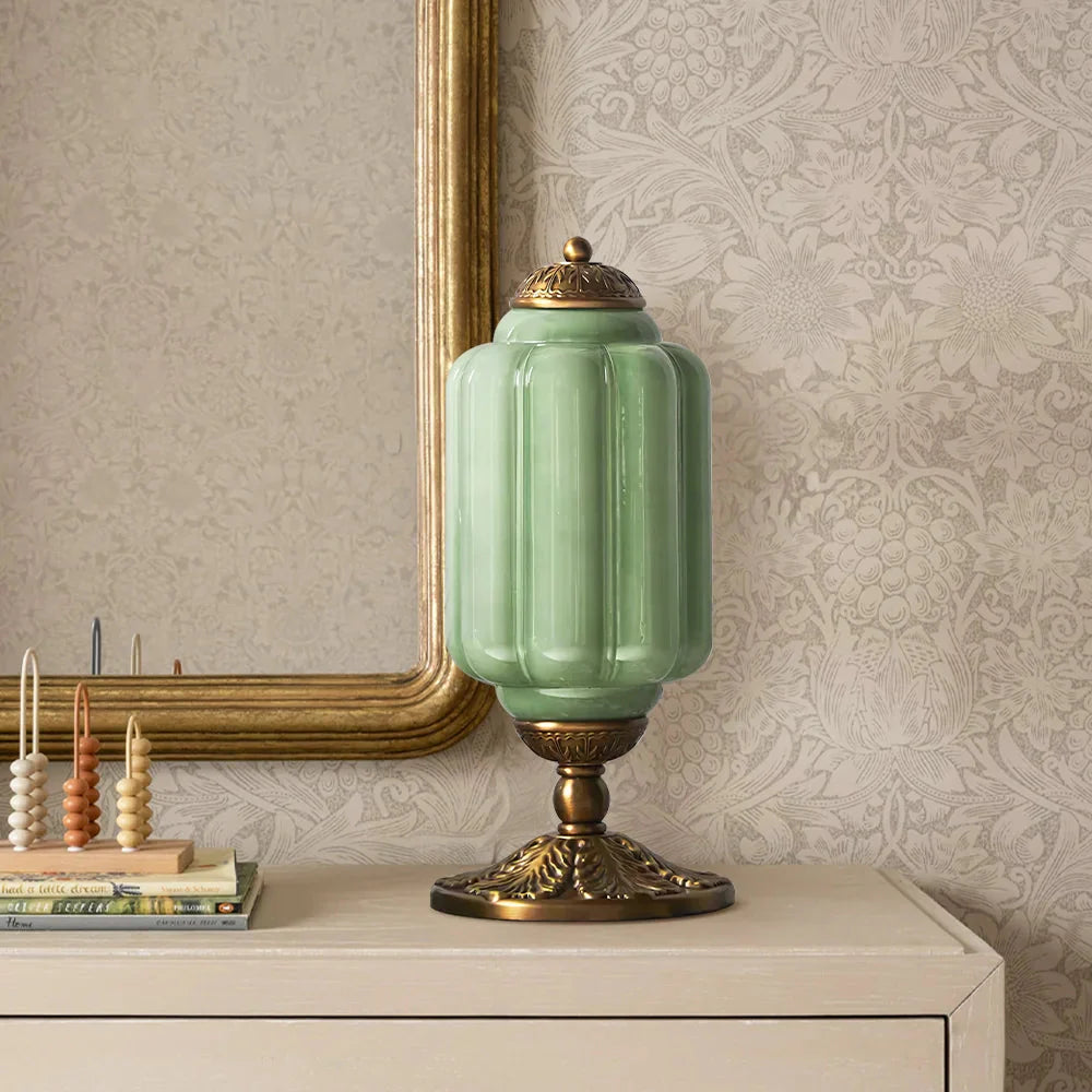 Decorative green lamp with gold base on a table against a patterned wall.