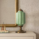 Decorative green lamp with gold base on a table against a patterned wall.