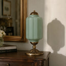 Decorative green lamp with gold base on a wooden surface, with books and a mirror in the background.
