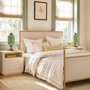 Neatly made bed with decorative pillows in a bright bedroom with two windows.