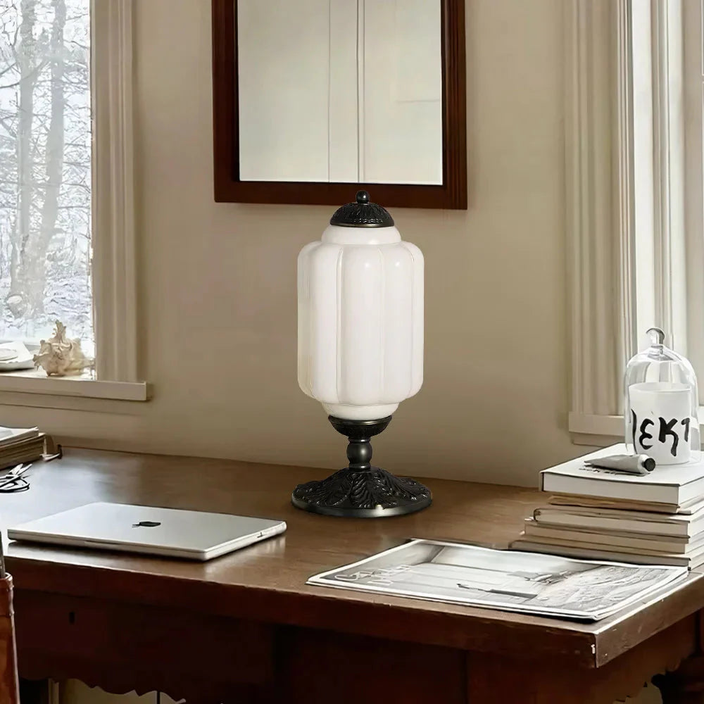 Table lamp on a desk with a laptop and books in a room with a window and mirror.
