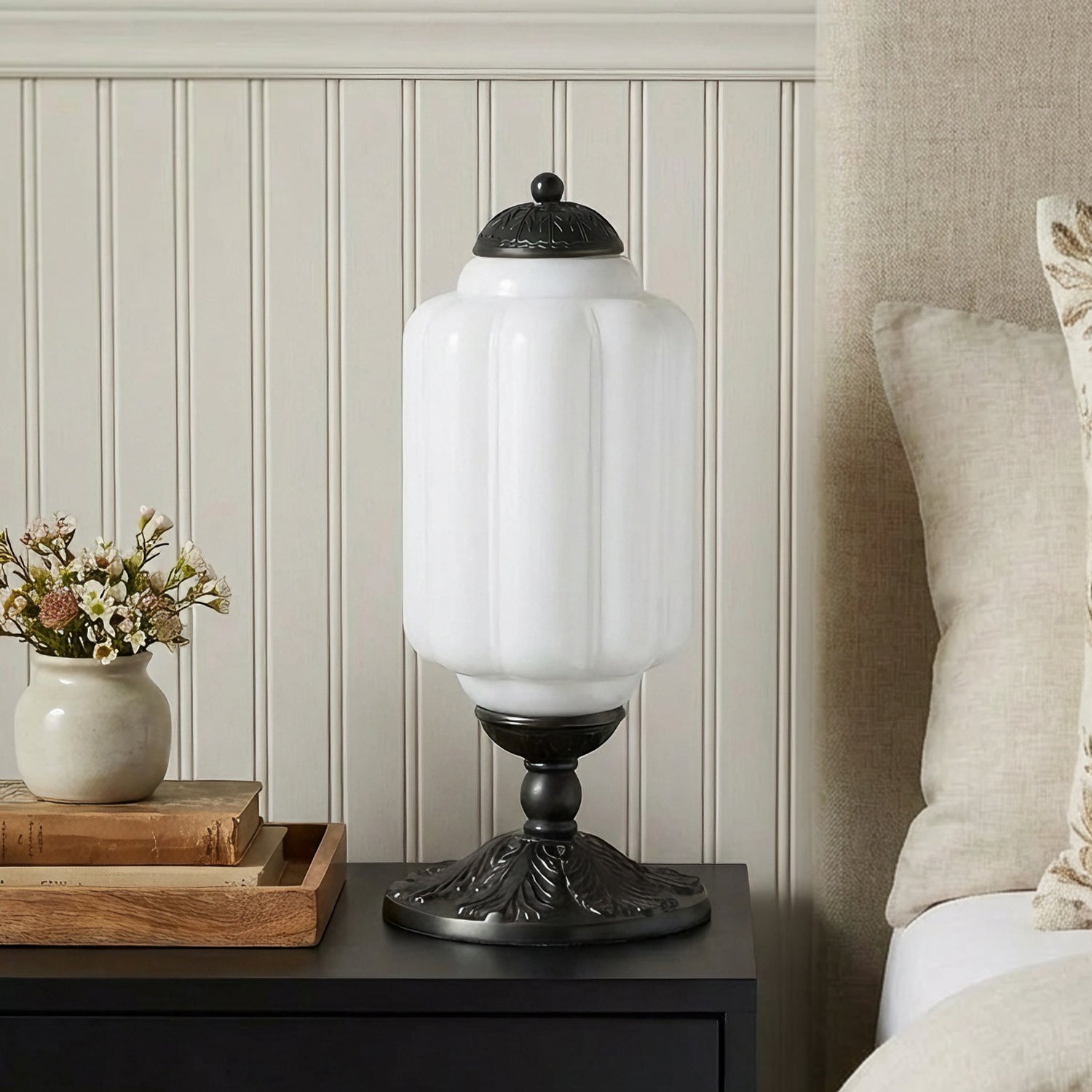 Decorative table lamp on a nightstand with floral arrangement and books in the background.