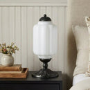 Decorative table lamp on a nightstand with floral arrangement and books in the background.