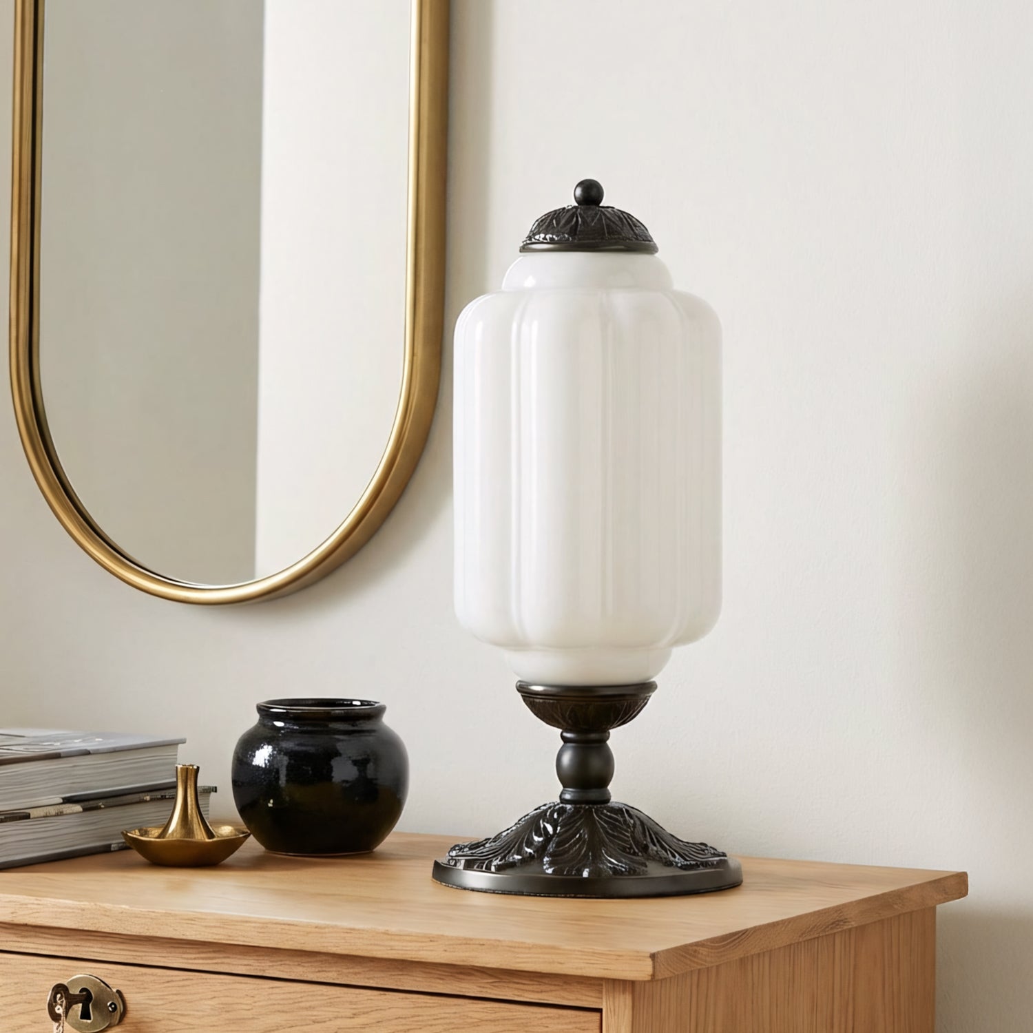 Decorative table lamp on a wooden surface with a mirror and books in the background.