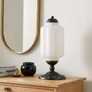 Decorative table lamp on a wooden surface with a mirror and books in the background.