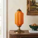 Decorative orange table lamp on a wooden surface with a painting in the background