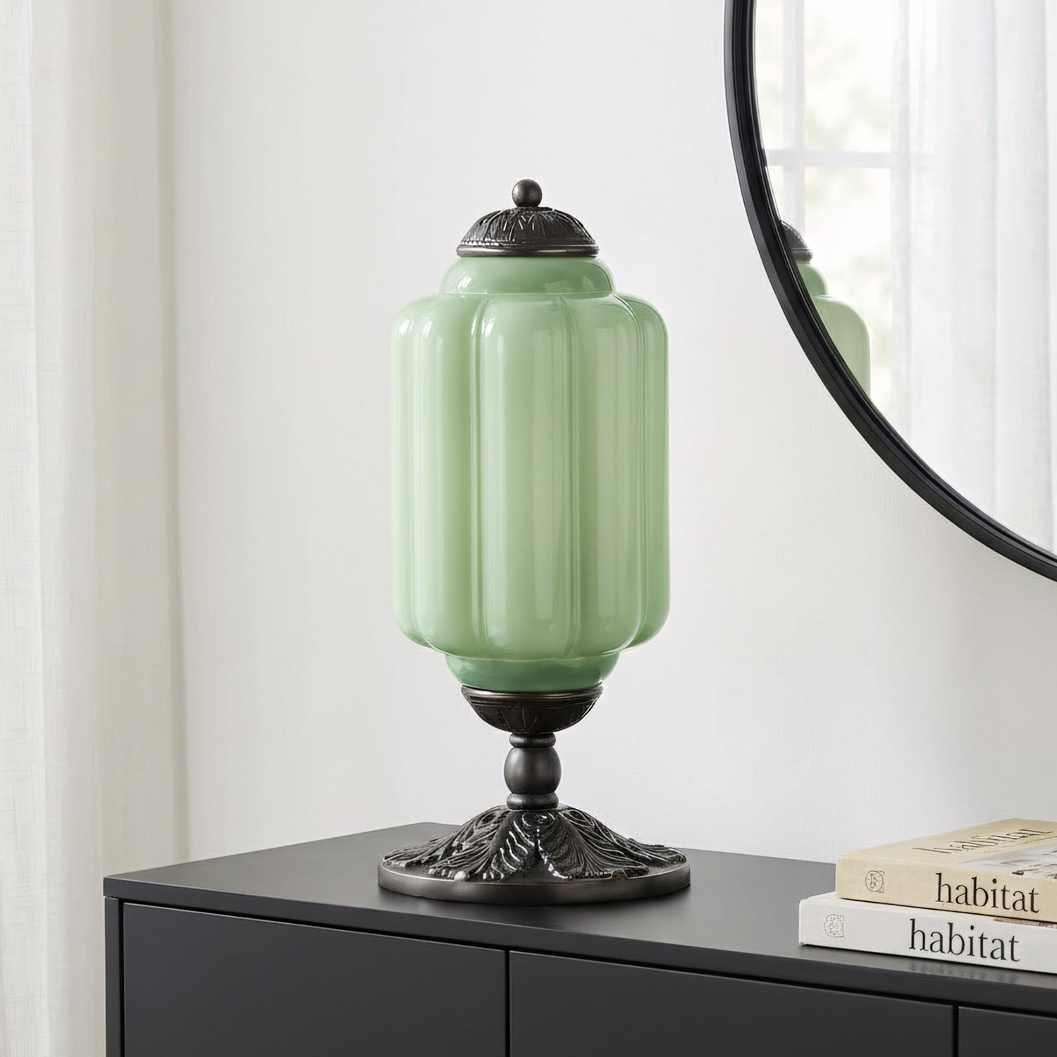 Green lamp with decorative base on a black surface next to a mirror