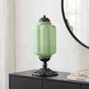 Green lamp with decorative base on a black surface next to a mirror