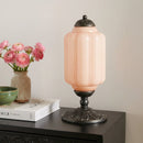 Vintage-style table lamp with pink glass shade on a dark surface next to books and flowers.