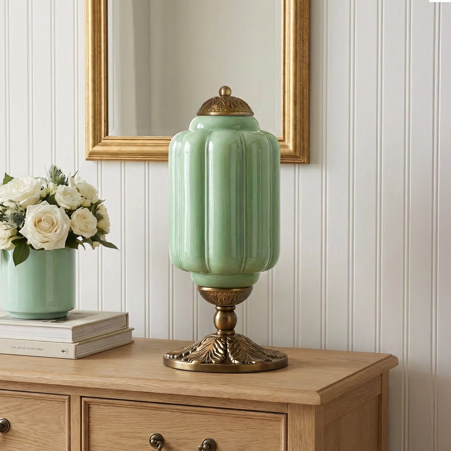 Green lamp with gold base on a wooden cabinet against a white paneled wall.