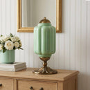 Green lamp with gold base on a wooden cabinet against a white paneled wall.