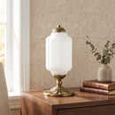 Decorative table lamp with white glass shade and gold base on a wooden surface.