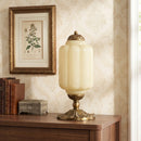 Decorative table lamp on a wooden surface with a framed botanical print in the background.