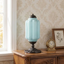 Decorative lamp with a blue glass shade on a wooden cabinet against a patterned wall.
