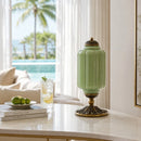 Decorative green lamp with gold base on a table by a window with a view of palm trees and a pool.
