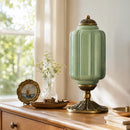 Decorative green lamp with gold base on a wooden surface near a window.
