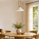 Dining room with a round wooden table, chairs, and a vase with greenery near a window.