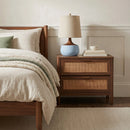 Wooden nightstand with a lamp next to a bed in a bedroom setting