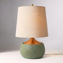 Table lamp with a textured green base and beige lampshade on a neutral background
