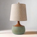 Table lamp with a textured beige shade and green base on a neutral background