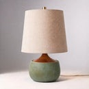Table lamp with a beige shade and green base on a neutral background