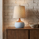 Table lamp with a textured shade on a wooden cabinet against a brick wall.