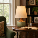 Table lamp on a wooden table with a book, glasses, and a glass of water in a cozy room.
