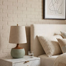Lamp on a nightstand next to a sofa with a glass of water, against a brick wall.