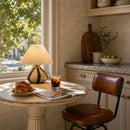 Small dining table with a plate of croissants, a glass of iced coffee, and an open magazine in a kitchen setting.