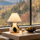 Decorative lamp on a table with a view of autumn trees outside a window.