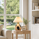 Decorative lamp on a side table in a living room with a window view of greenery.