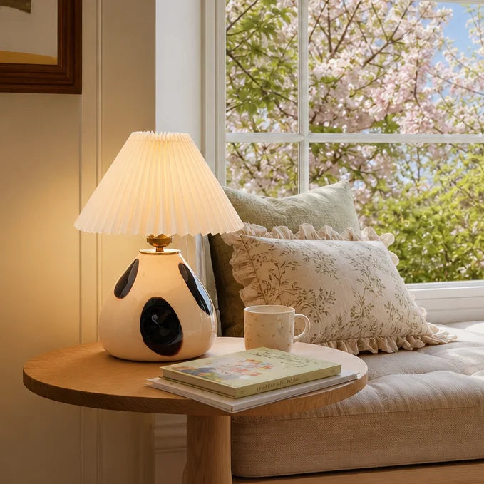 Lamp on a table next to a couch with pillows and a cup, with cherry blossoms outside the window.