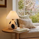 Lamp on a table next to a couch with pillows and a cup, with cherry blossoms outside the window.
