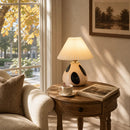 Cozy living room with a wooden side table, lamp, mug, and newspaper by a window with autumn foliage.