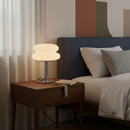 Bedroom scene with a nightstand, lamp, and bed with pillows.