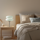 Neatly made bed with pillows and a blanket in a bedroom setting with a lamp on a nightstand.