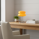 Yellow table lamp on a wooden desk with a chair and books in a room.